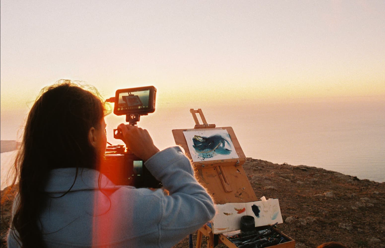 Photo of Giulia filming a painting set on the edge of a cliff, at sunset hour