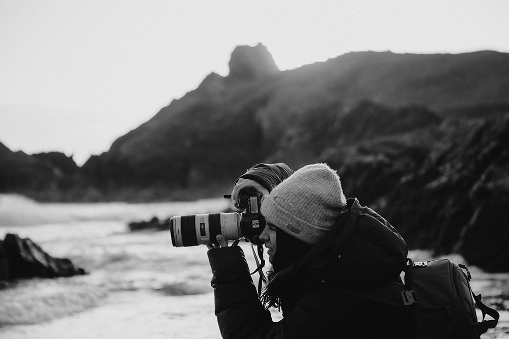 Black and white photo of Giulia taking a photo with a DSLR and a long zoom lens